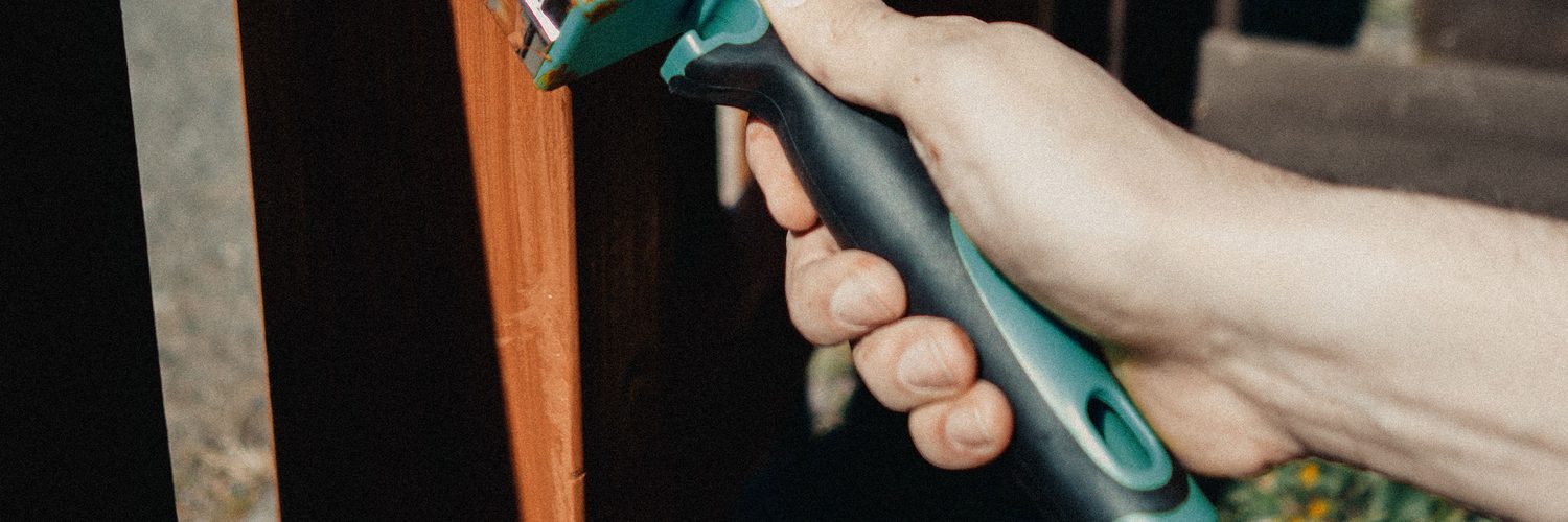 Close-up of a hand staining a wood fence